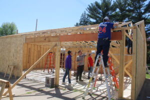 Construction trades students work under the supervision of their teacher to build a garage. 