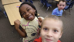 A little girl smiles at the camera alongside two boys