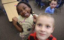 A little girl smiles at the camera alongside two boys