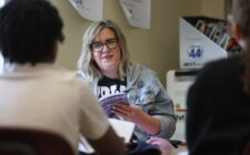 A paraeducator reads along to a book with a group of students
